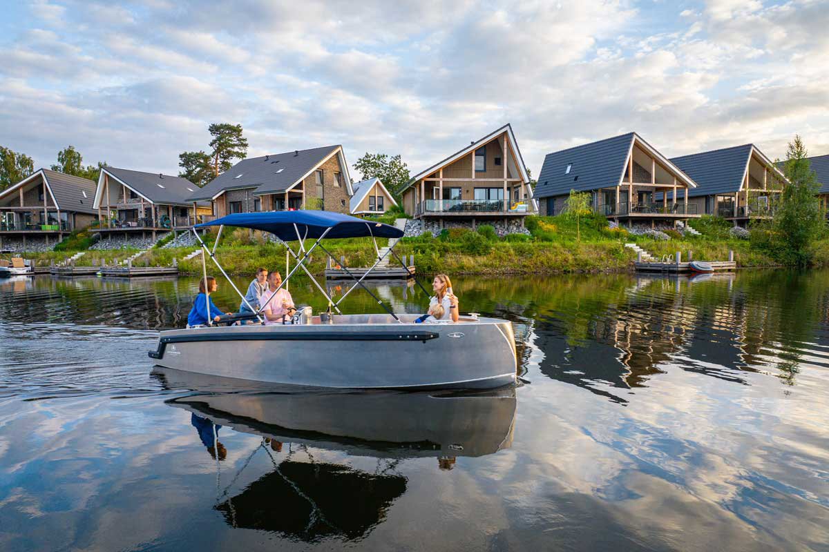 Familie bei einer Bootsfahrt auf dem See vor modernen Ferienhäusern im Landal Marina Resort Well – entspannter Wasserurlaub in den Niederlanden.