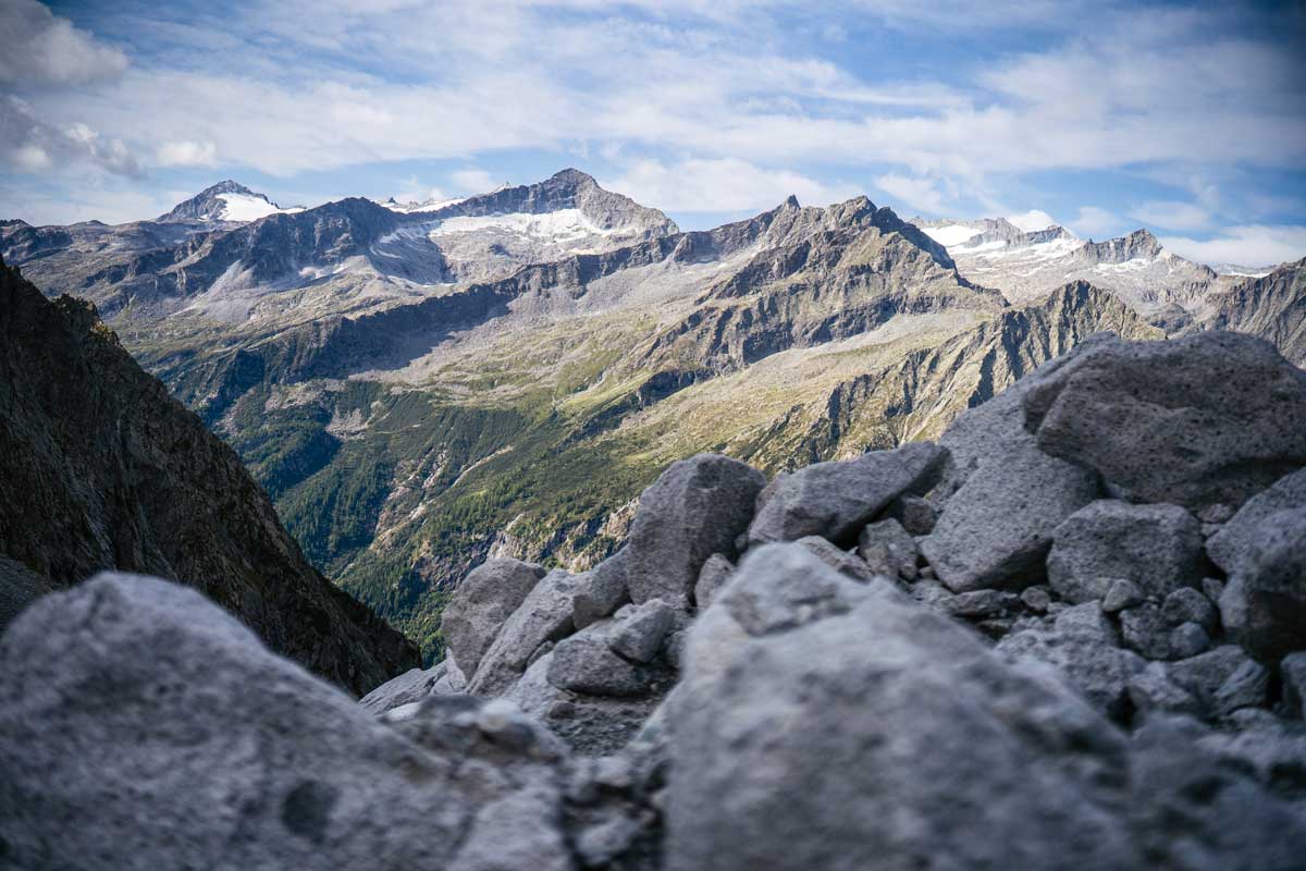 Blick auf die wilden Täler des Trentino entlang der Via delle Valli mit Felsen im Vordergrund und schroffen Alpen im Hintergrund.